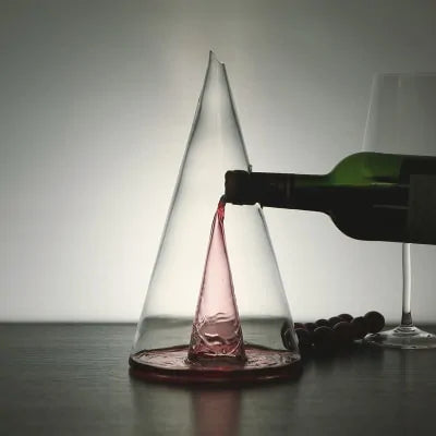 Transparent glass pyramid-shaped wine decanter with red wine being poured.