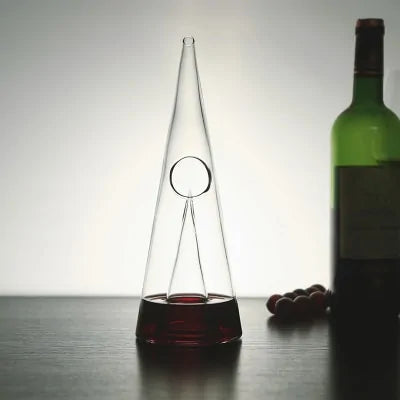 Transparent CrystalPyramid™ wine decanter with pyramid shape, elegant design, and wine bottle in background.